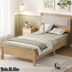 Natural wood Twin XL bed frame with upholstered headboard, three-quarter bedroom view